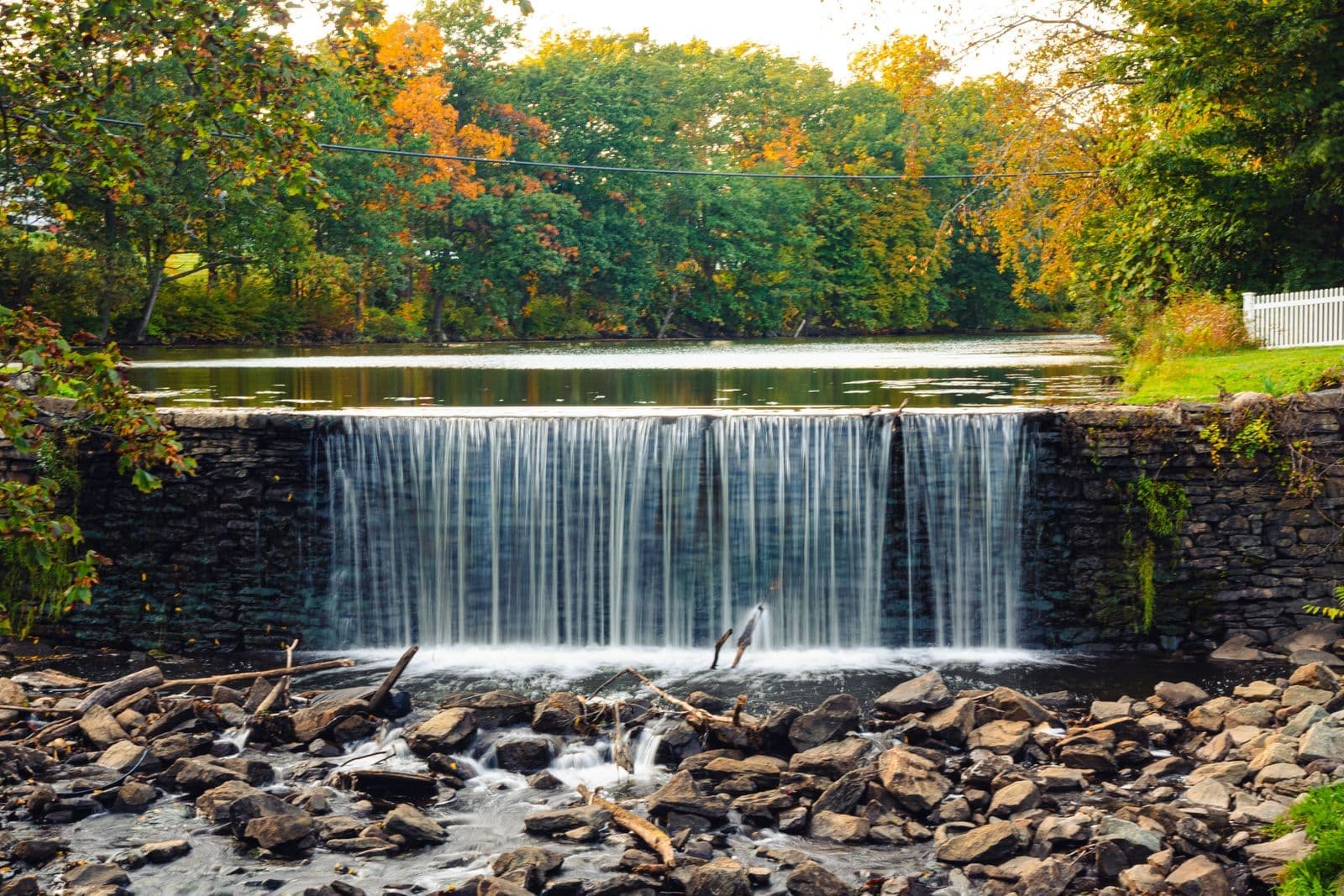 A low dam with water spilling over it on a river in autumn